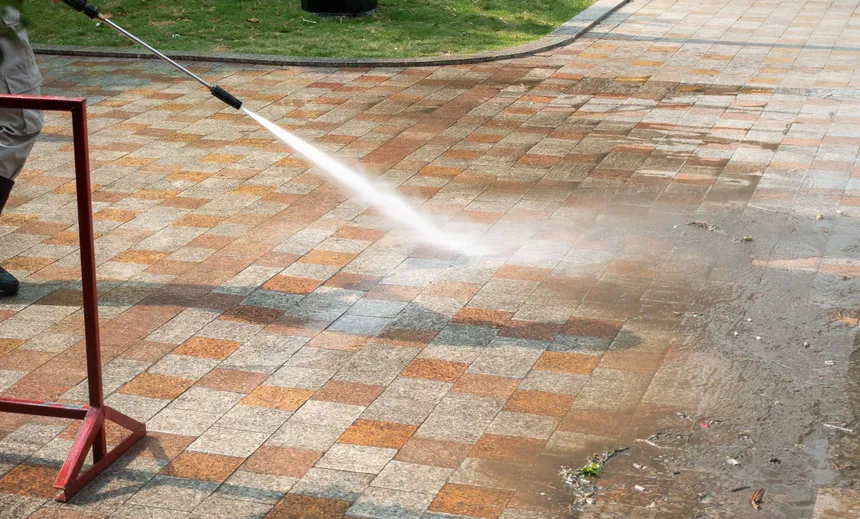 A pressure washer wand cleaning a paver driveway