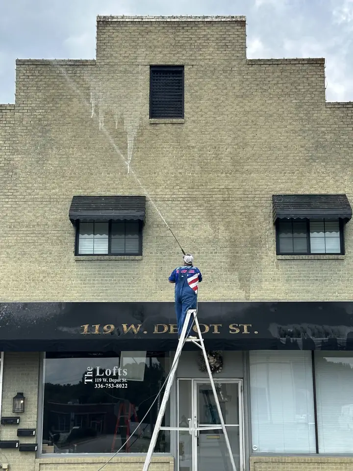 A worker on a tall ladder washing the brick front of a two story building on Depot Street
