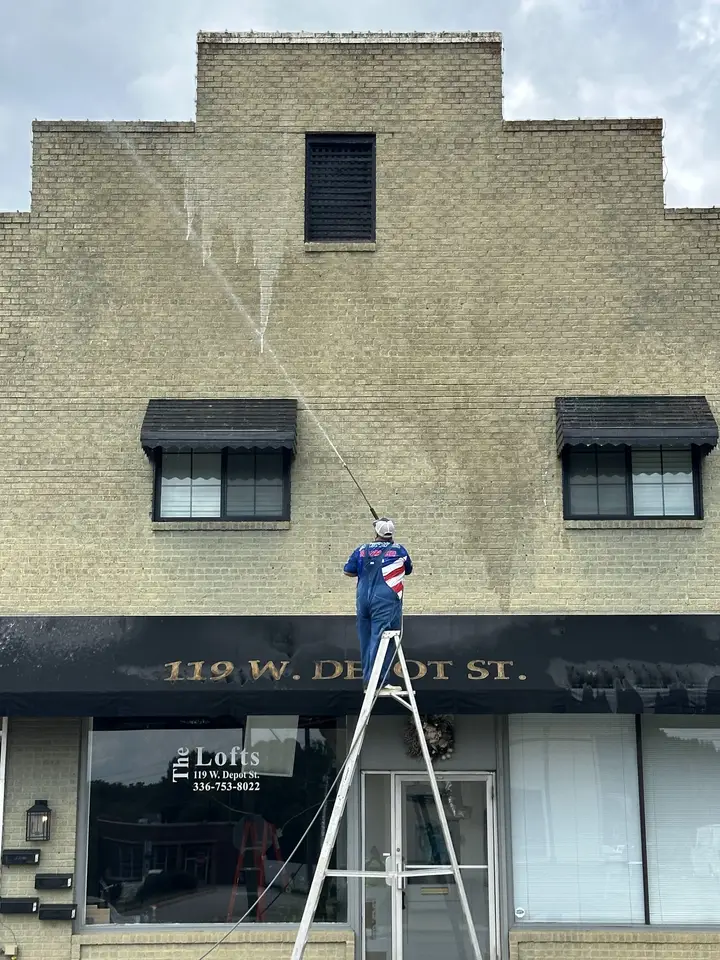 A worker on a tall ladder washing the brick front of a two-story downtown building