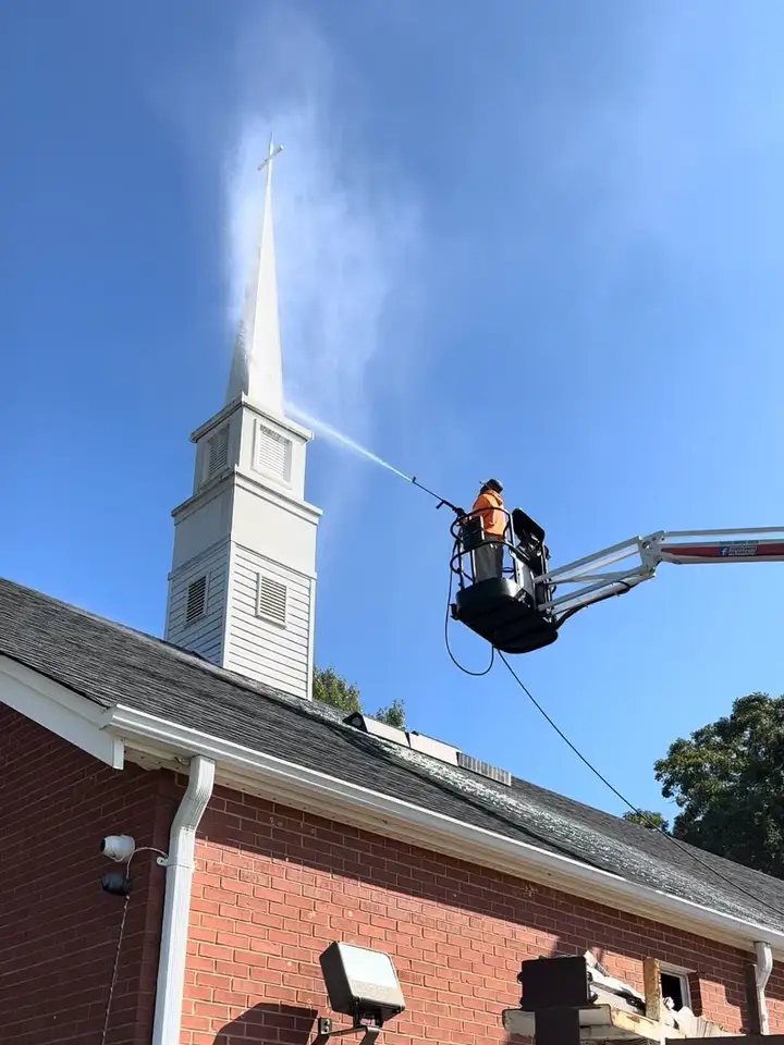 Spray arcing past the top of a white church steeple from a raised boom lift basket