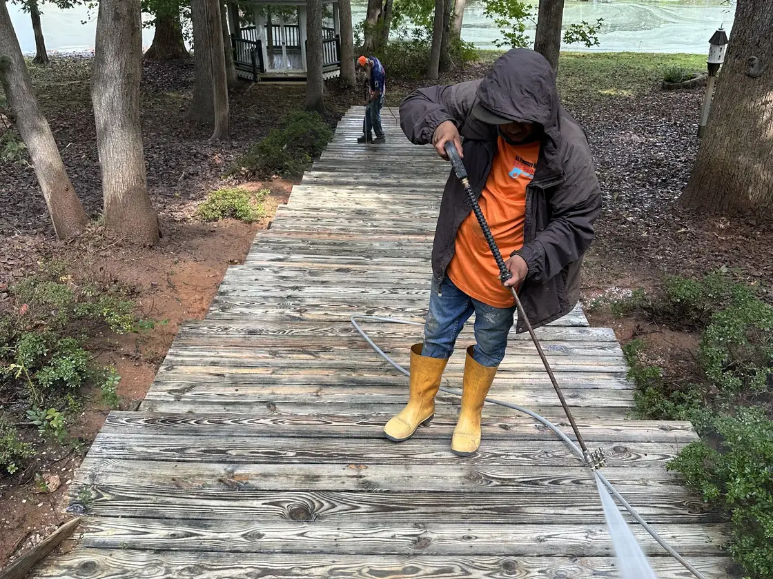 A worker in rubber boots running a wand down the boards of a lakeside boardwalk