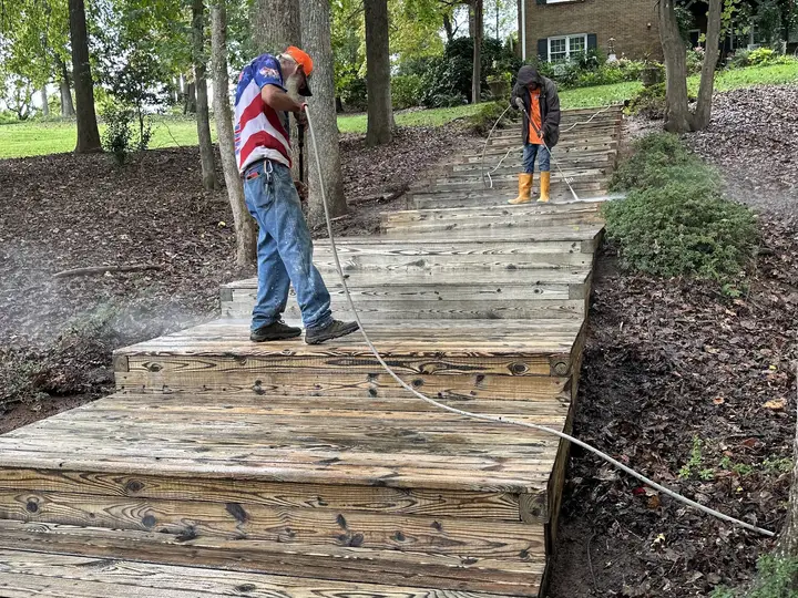 Two crew members washing the boards of a wooden walkway running down to a lake