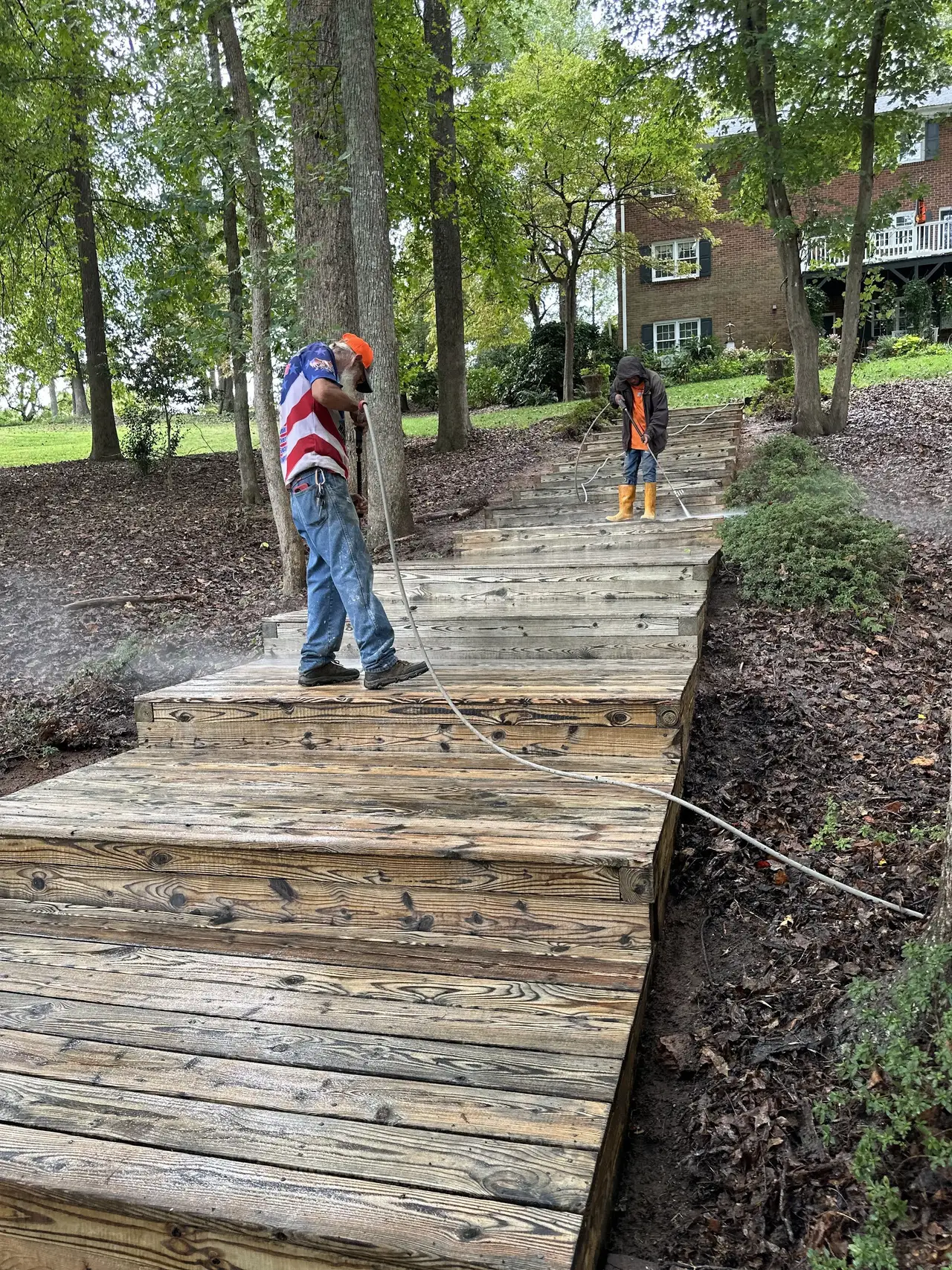 Two crew members washing the boards of a wooden walkway running down to a lake