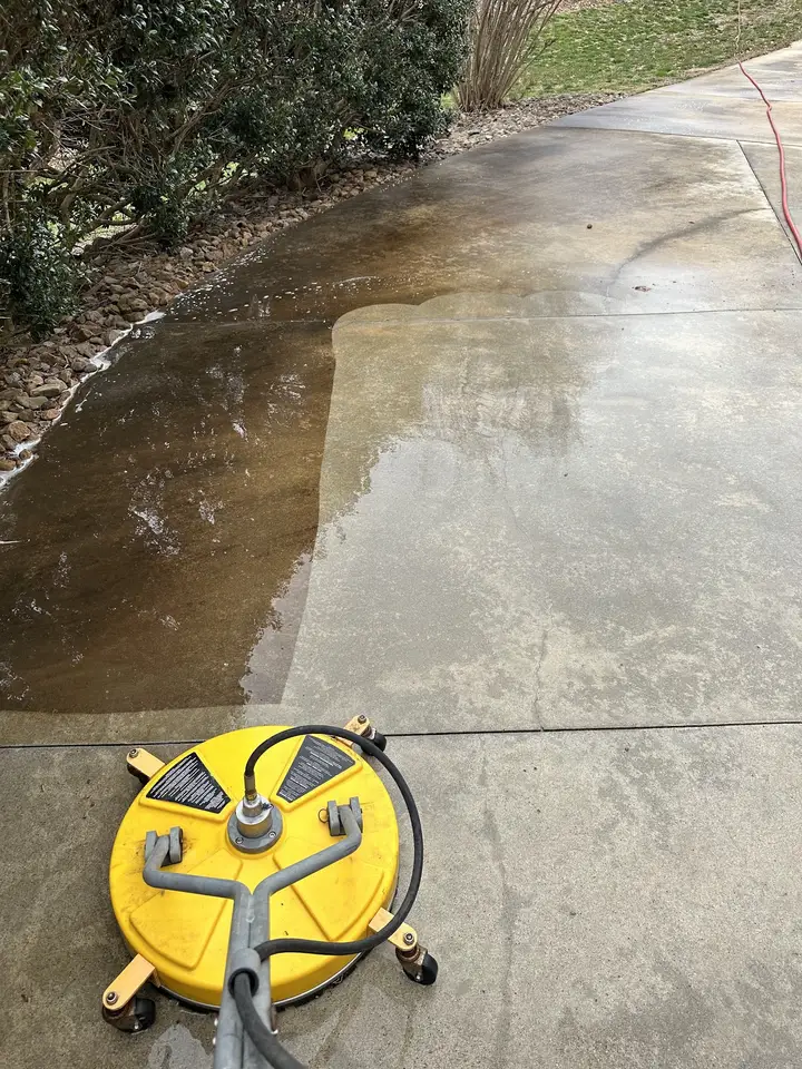 A concrete driveway half washed, with a hard line between the clean side and the dirty side and the surface cleaner still on it