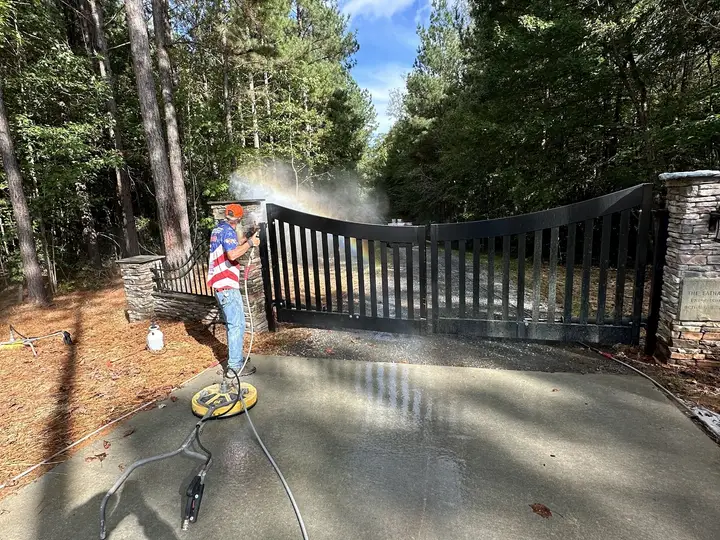 A crew member washing a long private lane in front of a black gate