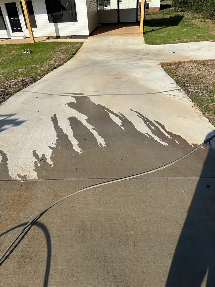 A wide concrete driveway with clean streaks fanned out across the dirty surface where the wash has started
