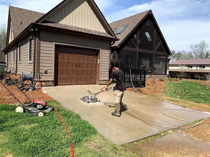 A crew member running a surface cleaner down the driveway of a craftsman home