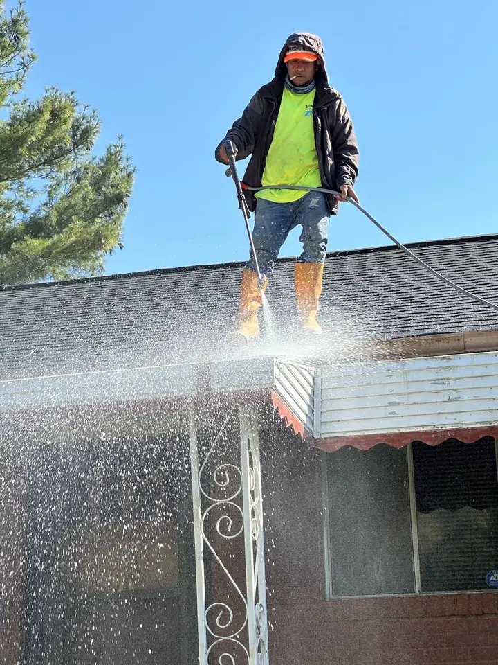 A worker standing at a roof edge washing down over a scalloped awning while water pours off it