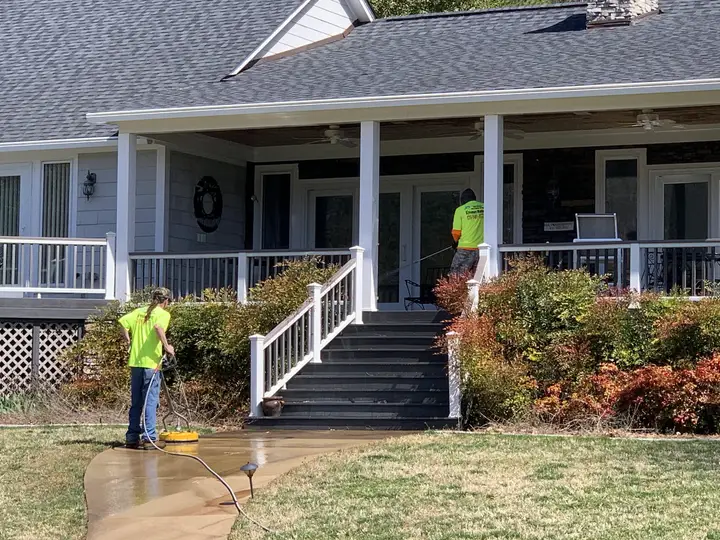 Two crew members washing a farmhouse porch, its rails and its front steps