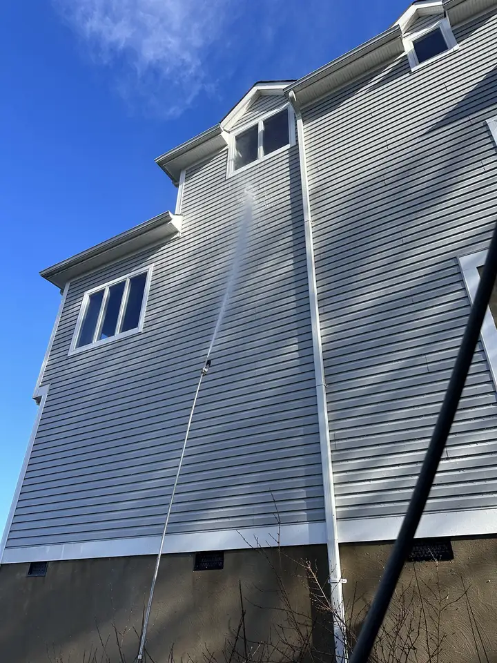 A long arc of water reaching the second story of a gray sided house from the ground