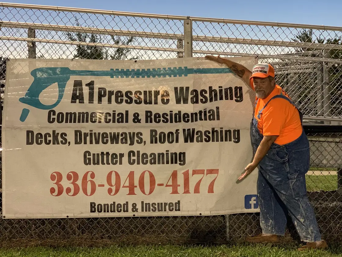 Robert in 2021 holding up the first A1 banner, hung on a chain link fence, with the company phone number across it