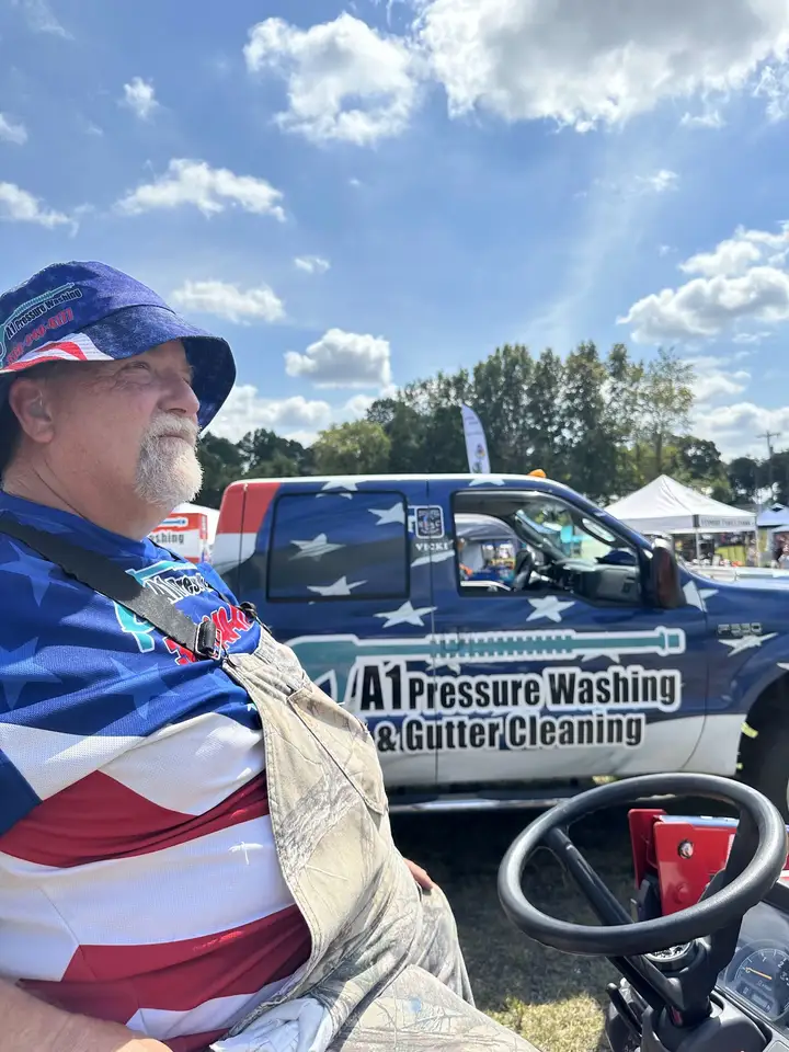 Robert in a stars and stripes bucket hat at an outdoor county event, with the flag wrapped A1 truck behind him