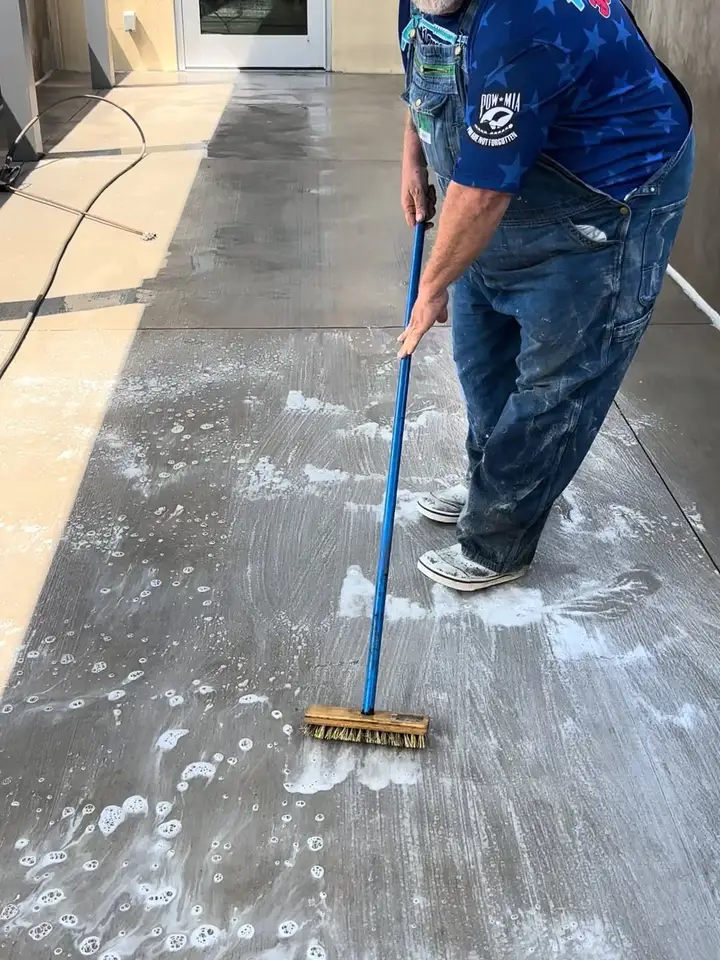 Robert scrubbing a soapy concrete walkway with a long push broom outside a storefront