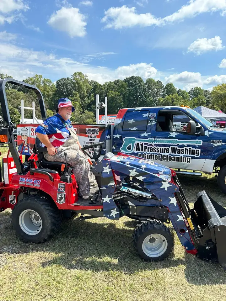 Robert on a red compact tractor at the fair, with the flag wrapped A1 truck and its services panel parked behind him