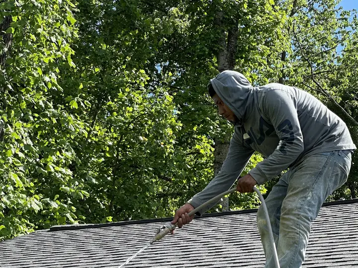 A crew member on a shingle roof washing it at low pressure