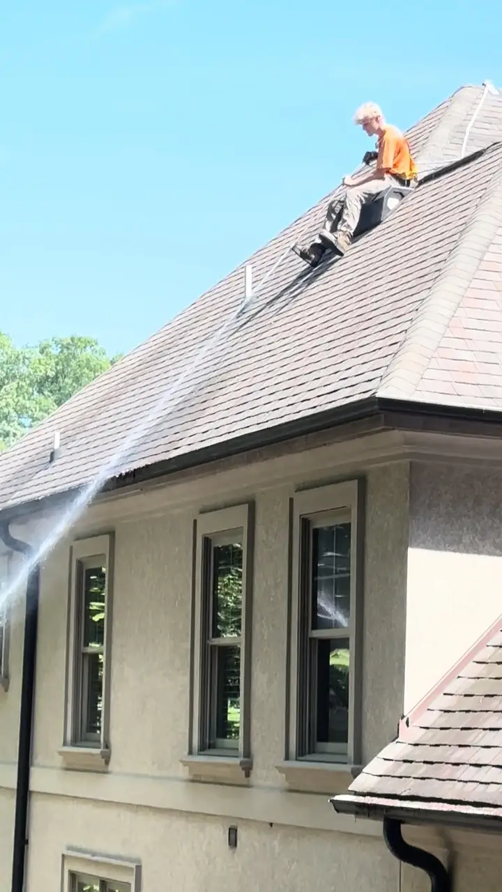 A crew member working from the ridge of a steep roof on a stucco house