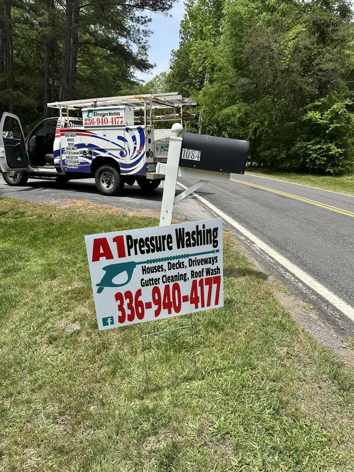An A1 Pressure Washing yard sign at the roadside with the truck parked in the driveway behind it